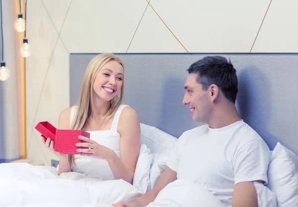 Pareja sonriente en la cama con caja de regalo roja — Foto de Stock