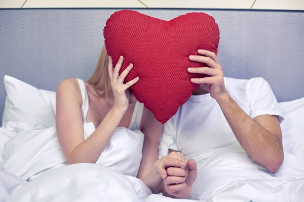 Casal feliz na cama com travesseiro em forma de coração vermelho — Fotografia de Stock
