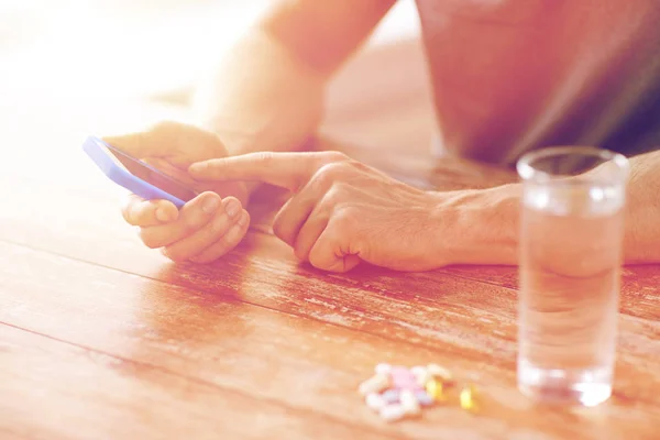 Close up of hands with smartphone, pills and water — Stock Photo, Image