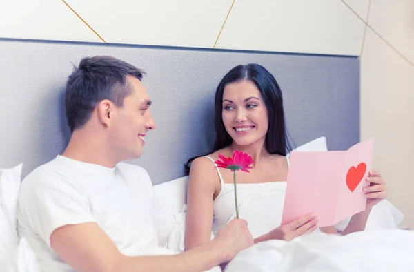 Couple souriant au lit avec carte postale et fleur — Photo