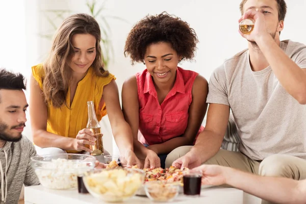 Amigos felizes com bebidas comer pizza em casa — Fotografia de Stock