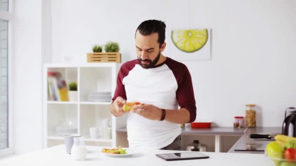 Чоловік з планшетним ПК їсть сніданок вдома — стокове відео