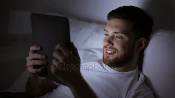 Młody człowiek z komputera typu tablet w łóżku w sypialni domu — Wideo stockowe