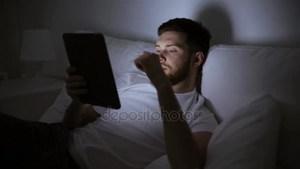 Молодий чоловік з планшетним ПК в ліжку в домашній спальні — стокове відео