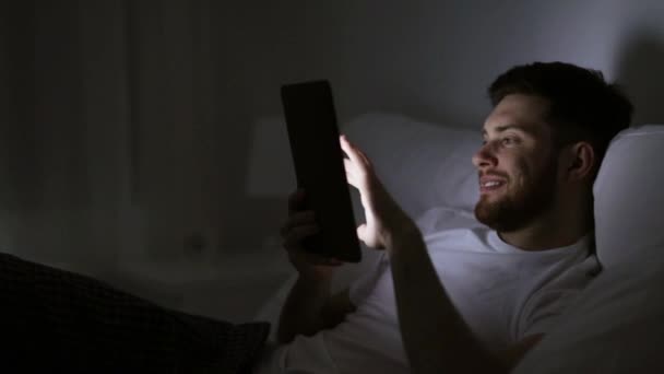 Молодий чоловік з планшетним ПК в ліжку в домашній спальні — стокове відео