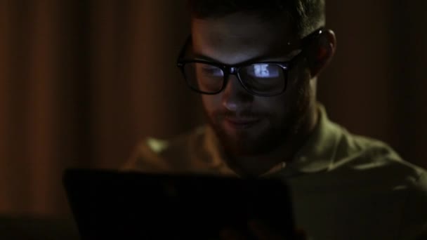 Молодой человек с планшетным компьютером, работающим в сети по ночам — стоковое видео