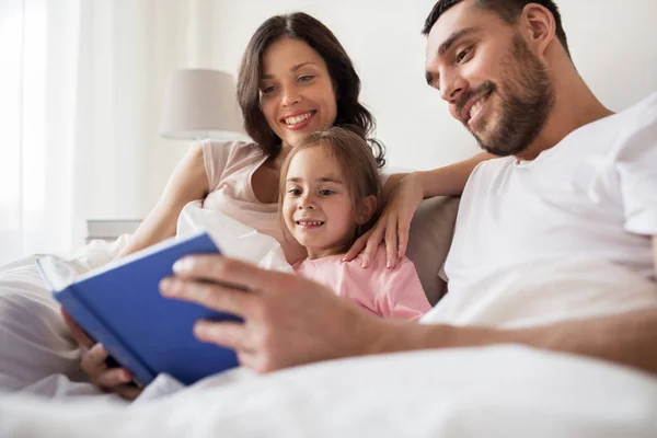 Happy family reading book in bed at home — Stock Photo, Image
