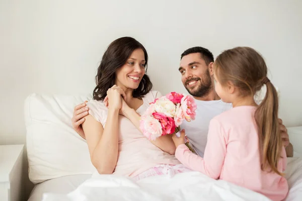 Šťastná dívka dávat květiny matce v posteli doma Stock Obrázky
