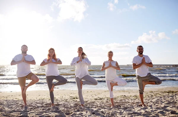 Grupa osób zarabiających jogi w drzewa ułożenia na plaży — Zdjęcie stockowe