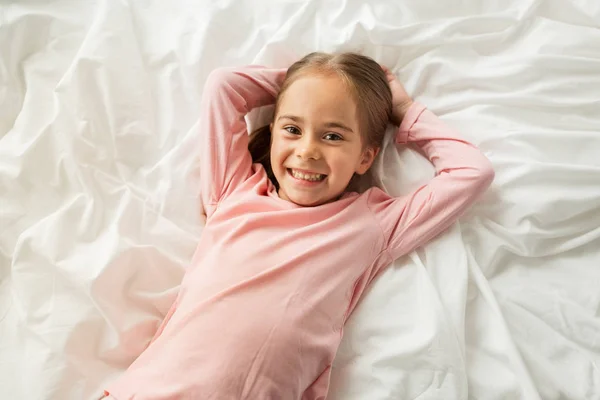 Счастливая маленькая девочка, лежащая в постели дома — стоковое фото