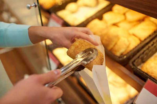Mano con pinzas tomando bollo en panadería o supermercado —  Fotos de Stock
