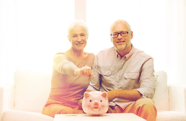 Casal sênior com dinheiro e banco porquinho em casa — Fotografia de Stock