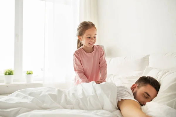 Little girl waking her sleeping father up in bed — Stock Photo, Image