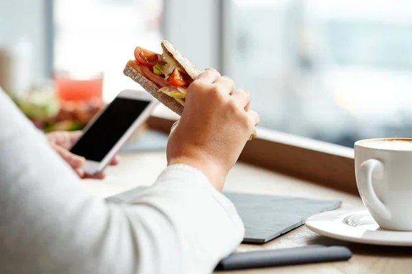 Mulher com smartphone e sanduíche no restaurante — Fotografia de Stock