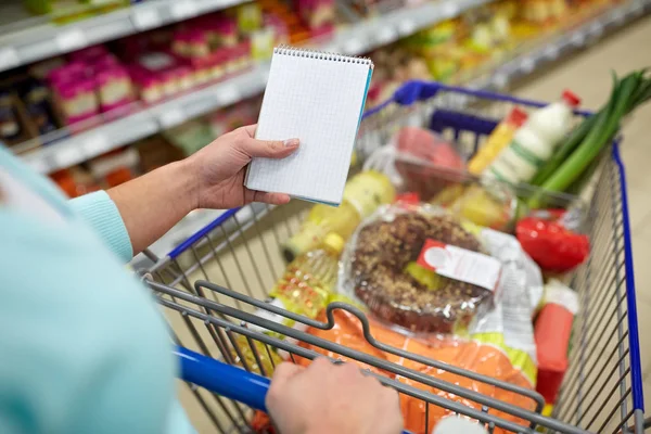Vrouw met voedsel in winkelwagen bij supermarkt — Stockfoto