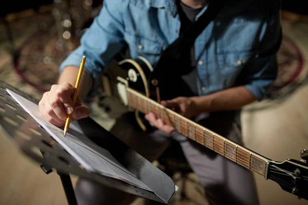 Uomo con chitarra iscritto a libro di musica in studio — Foto Stock