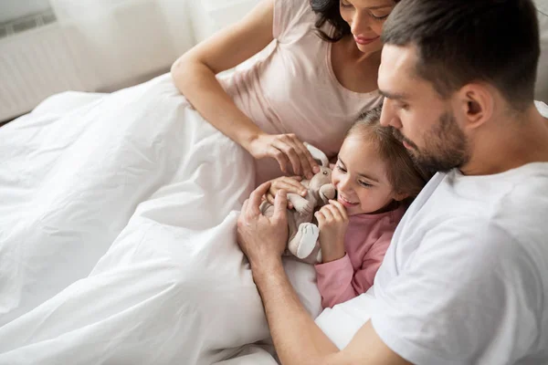 Bambino felice con giocattolo e genitori a letto a casa — Foto Stock