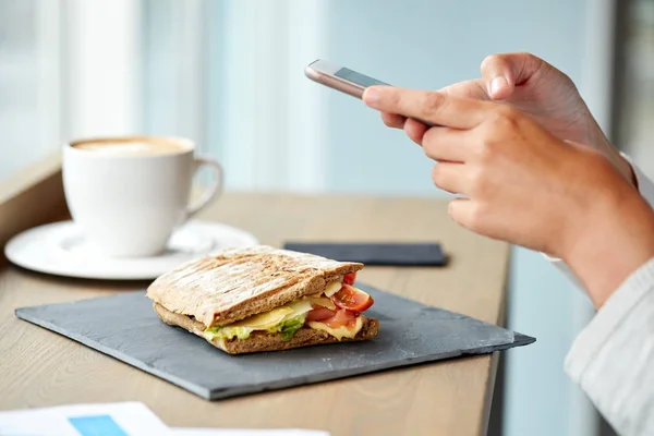 Сэндвич с панини и женщина со смартфоном в кафе — стоковое фото