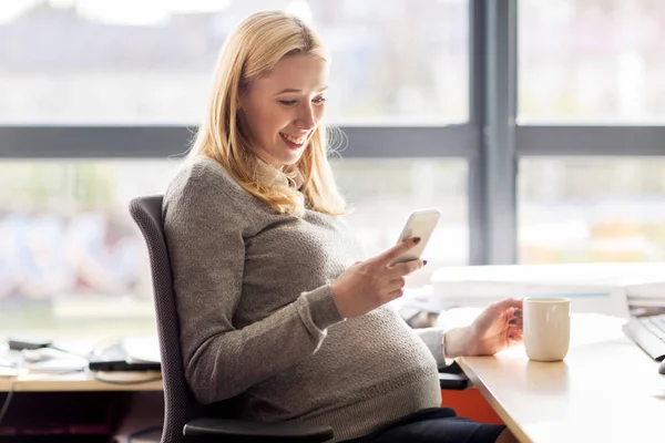 Mujer de negocios embarazada con teléfono inteligente en la oficina — Foto de Stock