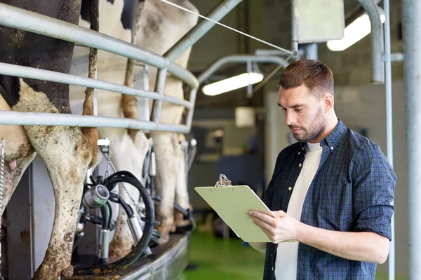 Hombre con portapapeles y vacas lecheras en la granja lechera — Foto de Stock