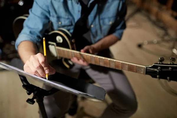 Uomo con chitarra iscritto a libro di musica in studio — Foto Stock