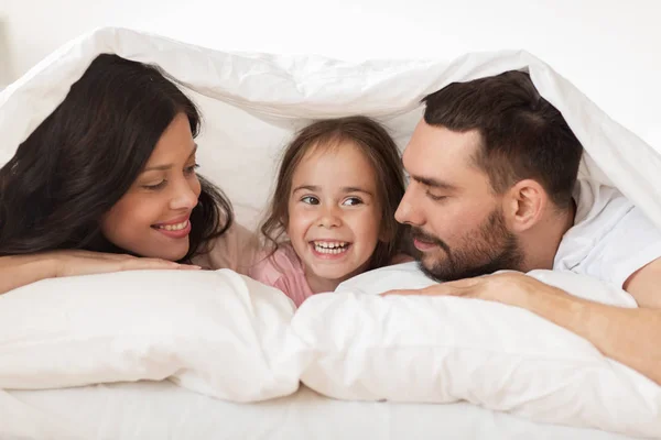 Szczęśliwa rodzina leżąc w łóżku pod koc w domu — Zdjęcie stockowe