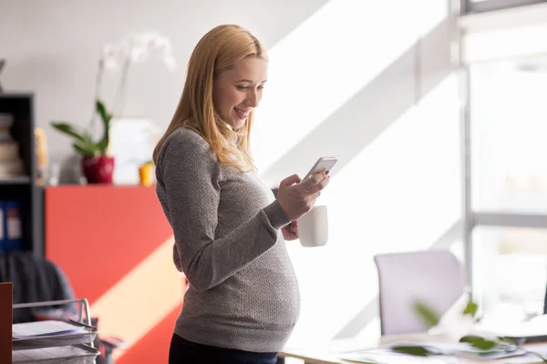 Femme d'affaires enceinte avec smartphone au bureau — Photo