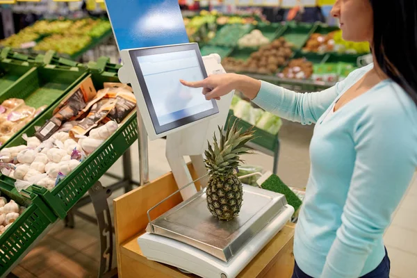 Vrouw met een gewicht van ananas op schaal in supermarkt — Stockfoto