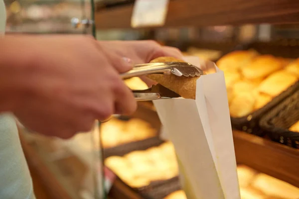 Hand met de Tang nemen broodje bij de bakker of supermarkt Stockafbeelding
