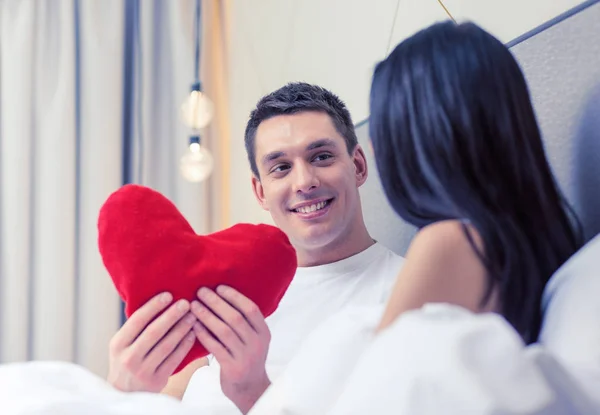 Lachende paar in bed met rood hart vorm kussen — Stockfoto