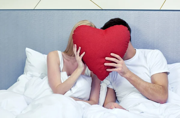 Feliz pareja en la cama con almohada en forma de corazón rojo —  Fotos de Stock