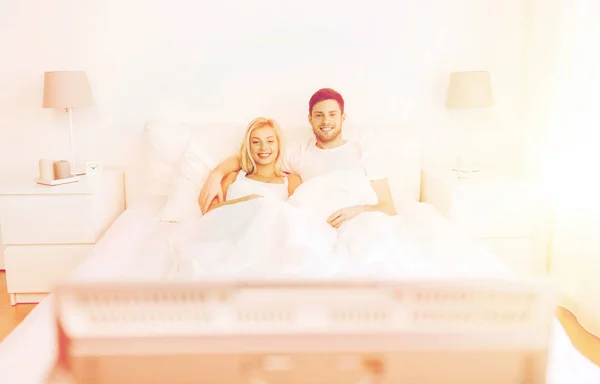 Feliz pareja acostada en la cama en casa y viendo la televisión — Foto de Stock