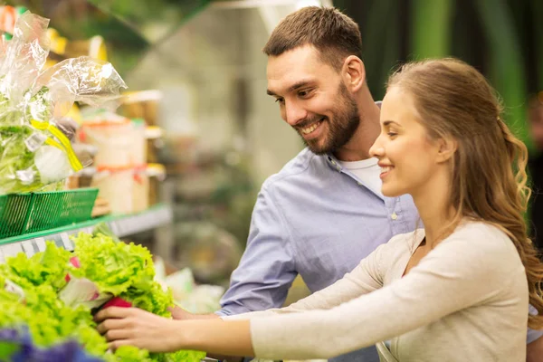 Happy couple buying lettuce at grocery store — Stock Photo, Image