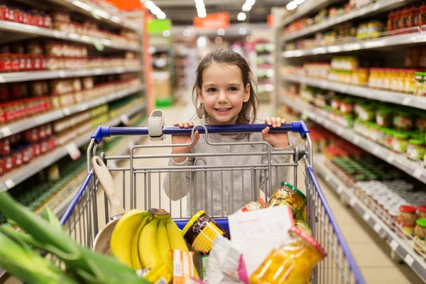 Chica con comida en el carrito de la compra en la tienda de comestibles — Foto de Stock