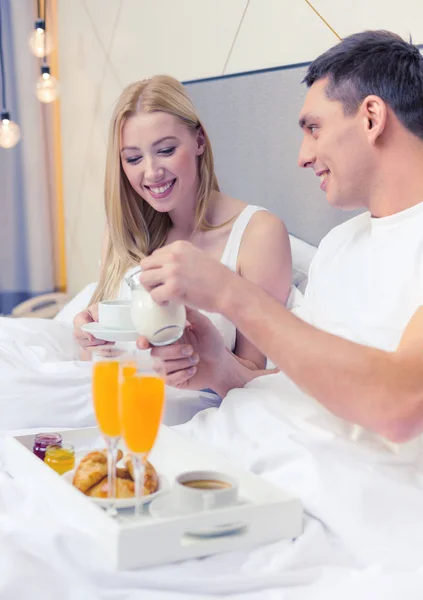 ホテルのベッドで朝食を持っている笑みを浮かべてカップル — ストック写真
