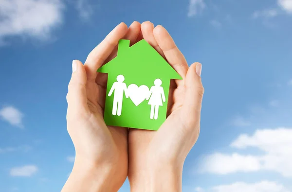 Mãos segurando casa verde com pictograma de família — Fotografia de Stock