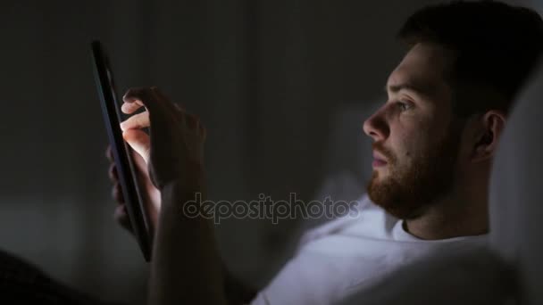 Hombre joven con tableta pc en la cama en el dormitorio en casa — Vídeos de Stock