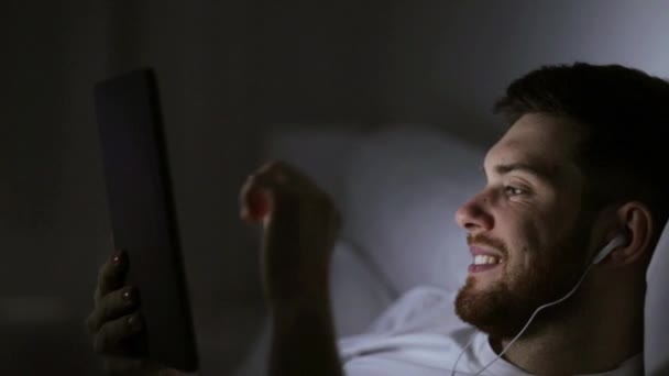 Muž s tablet pc a sluchátka v posteli v noci — Stock video