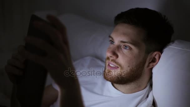 Jeune homme avec tablette PC dans le lit à la maison chambre — Video