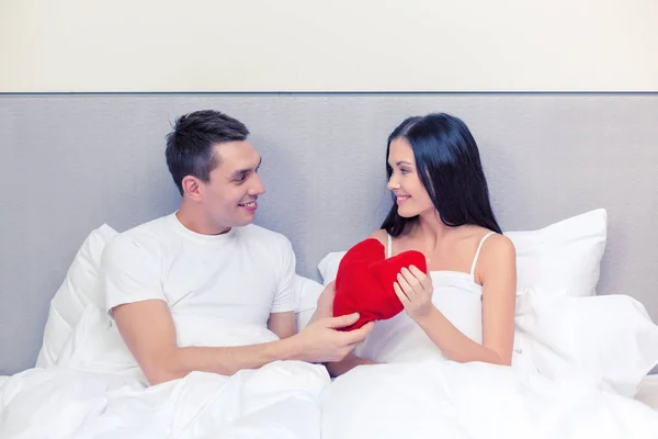 Pareja sonriente en la cama con almohada roja en forma de corazón — Foto de Stock