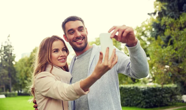 Casal feliz com smartphone tomando selfie no parque — Fotografia de Stock