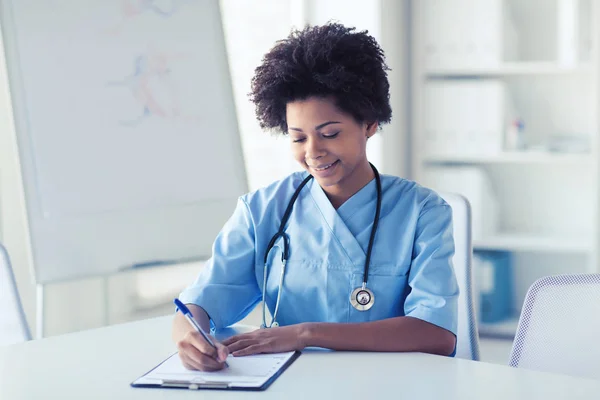 Lyckliga kvinnliga läkare eller sjuksköterska skriva till Urklipp — Stockfoto