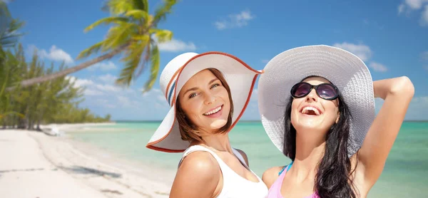 Glückliche junge Frauen mit Hüten am Sommerstrand — Stockfoto