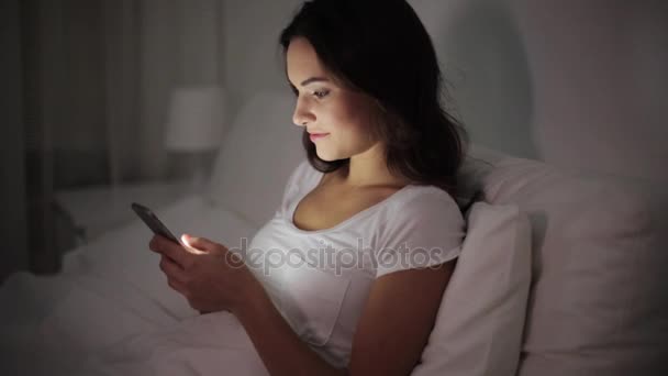 Šťastná mladá žena s smartphone v posteli v noci — Stock video