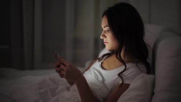 Женщина в постели со смартфоном собирается спать — стоковое видео