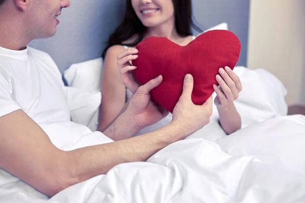 Pareja sonriente en la cama con almohada roja en forma de corazón — Foto de Stock