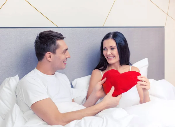 Coppia sorridente a letto con cuscino a forma di cuore rosso — Foto Stock