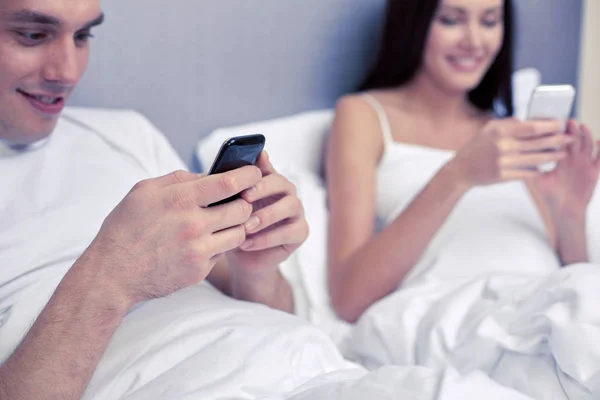 Close up of smiling couple in bed with smartphones — Stock Photo, Image