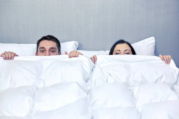 Feliz casal escondido sob cobertor na cama — Fotografia de Stock