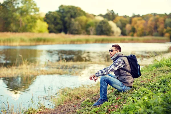 Man with backpack resting on river bank — Stock Photo, Image